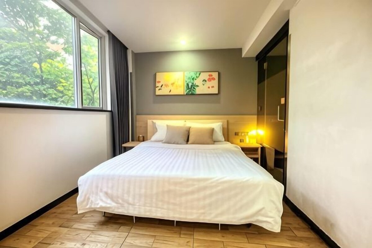 Een hotelkamer met een groot bed, nachtkastje, wandlamp en een raam met gordijnen.