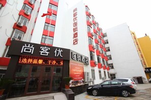 A hotel with a prominent red and white facade, a visible entrance with a signboard, and a parked car in front. - Shankee Hotel (Qingdao Development Zone Xiangjiang Second Road) (Qingdao)