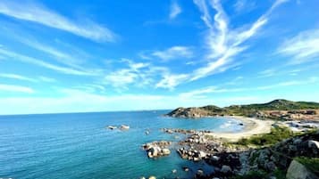 Un paisaje costero con costa rocosa, cielo azul despejado y colinas distantes.