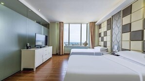 Habitación de hotel con una cama grande, televisión, cómoda y vistas a la ciudad.