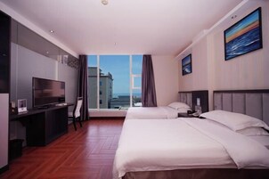 Habitación de hotel con un ventanal grande, un escritorio con televisor, dos camas y un cuadro en la pared.