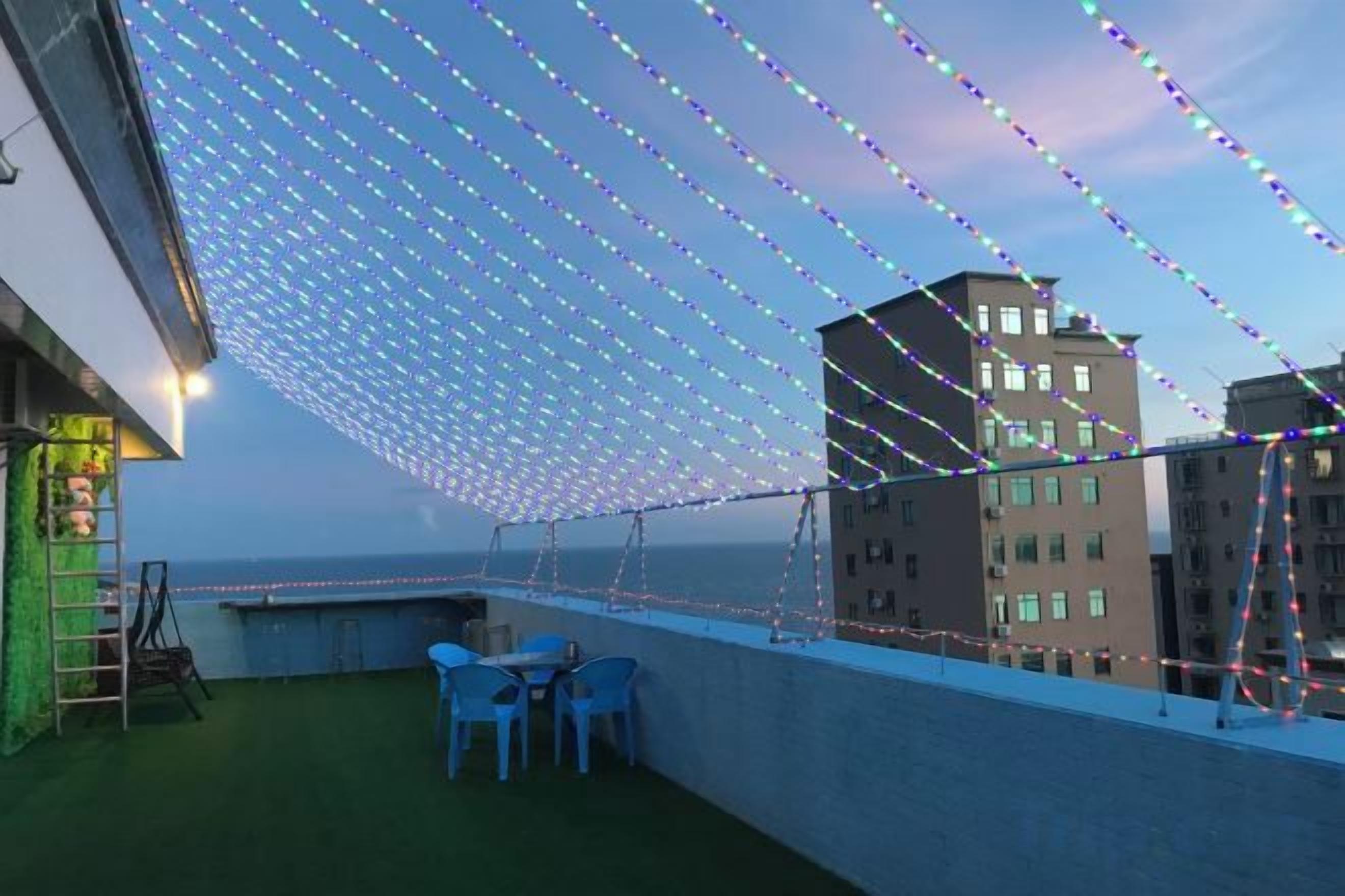 A rooftop terrace with a view of buildings, a green artificial turf, and blue chairs.