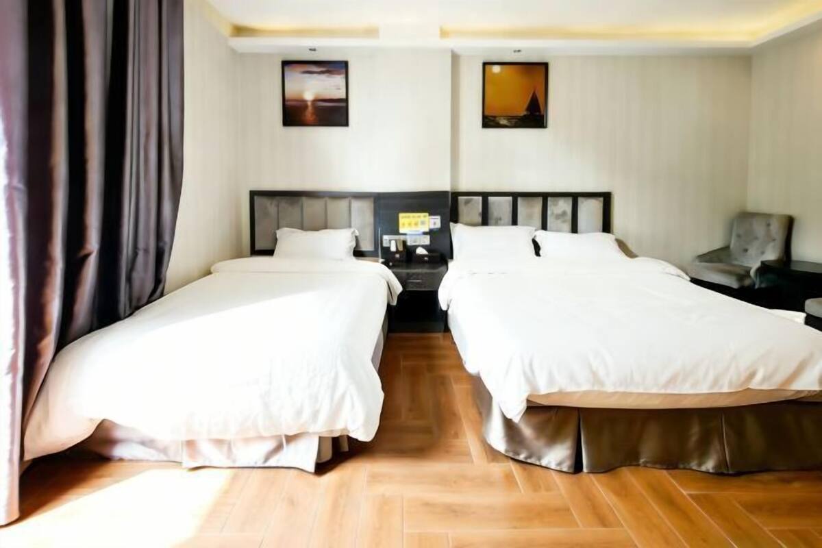Habitación de hotel con dos camas, una mesita de noche, una silla y dos cuadros en la pared.