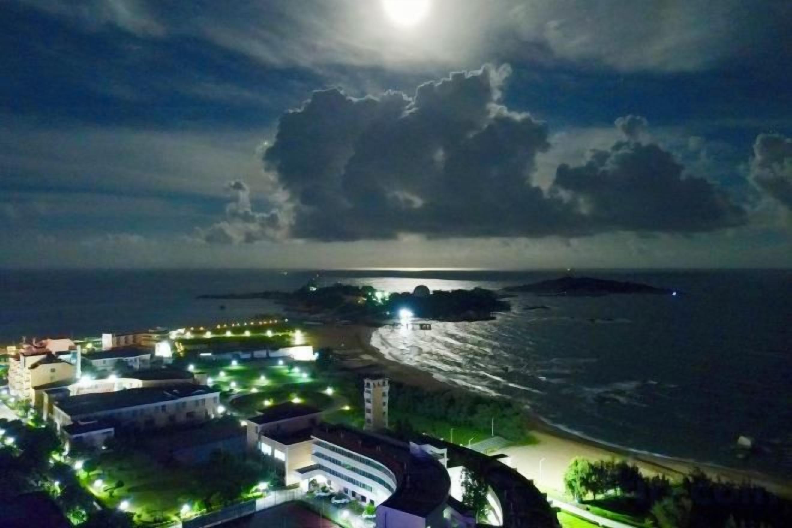 Vista costera con edificios, una playa y una extensión de agua bajo un cielo nublado.