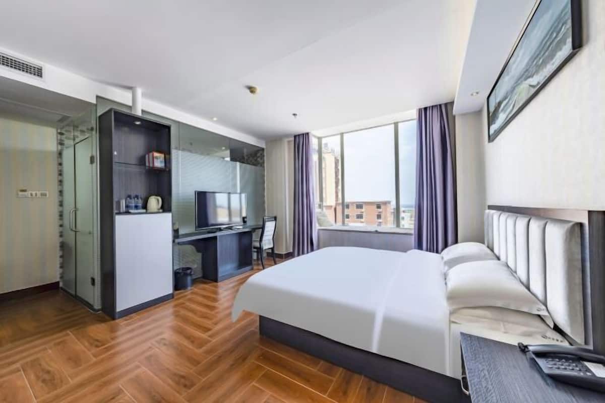 Habitación de hotel con cama, escritorio, silla, televisión y ventana con cortinas.