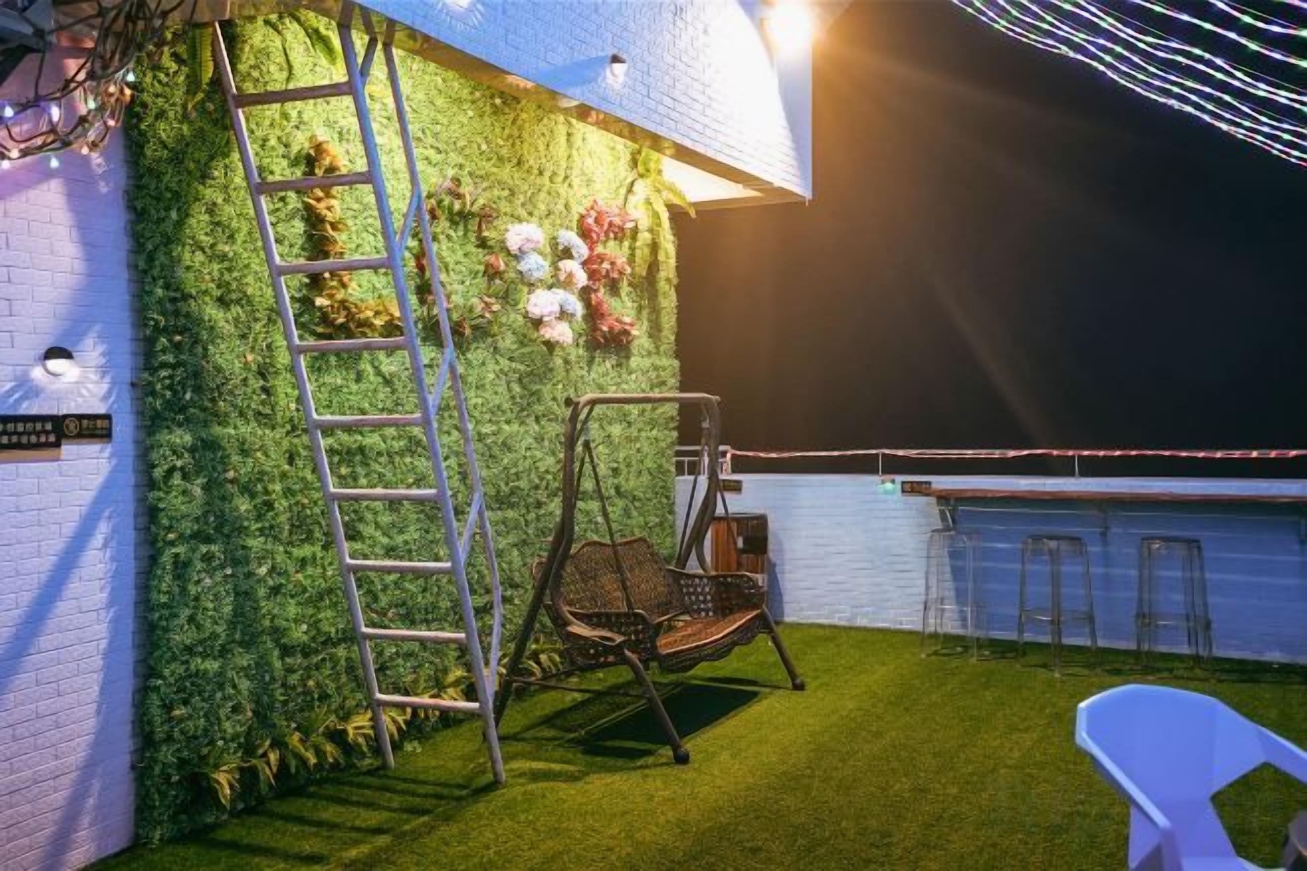A rooftop terrace with a green wall, a swing chair, a white chair, and a ladder.