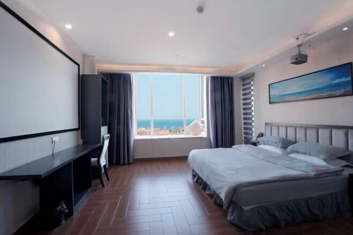 Habitación de hotel con cama, escritorio, ventana grande con vistas y un cuadro en la pared.