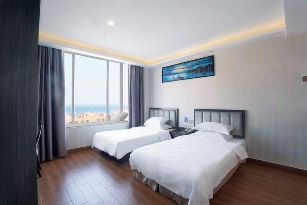 Habitación de hotel con dos camas, un cuadro en la pared y vistas de la ciudad a través de amplios ventanales.