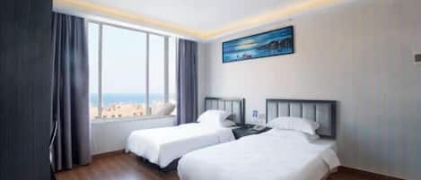 Habitación de hotel con dos camas, un cuadro en la pared y vistas de la ciudad a través de amplios ventanales.