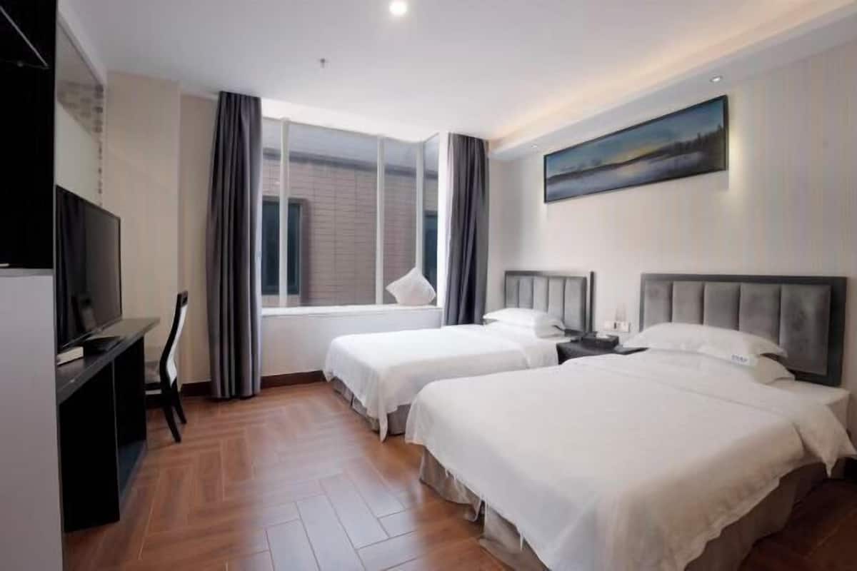Habitación de hotel con dos camas, televisión, ventana con cortinas y un cuadro en la pared.