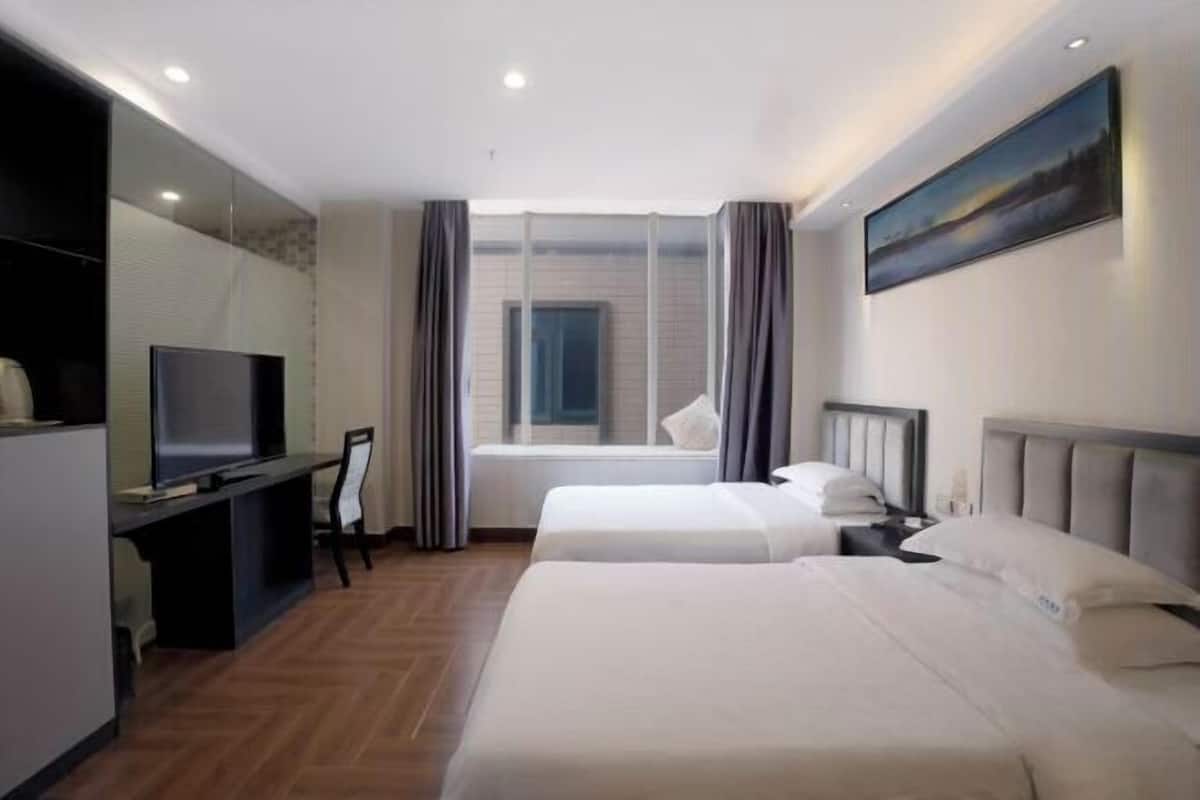 Habitación de hotel con dos camas, televisión, escritorio y ventana con cortinas.