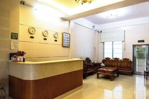 A reception area with a reception desk, wall clocks, a bulletin board, and a seating area with wooden furniture. - Riyuehe Hostel (Beihai)