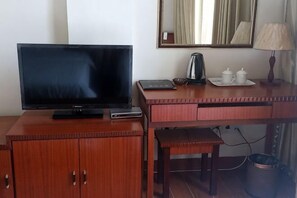 A hotel room with a television on a wooden cabinet, a desk with a lamp, and a trash bin. - Riyuehe Hostel (Beihai)