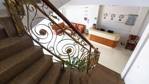 A staircase with ornate metal railings leading to a reception area with a counter and a brown leather couch. - Riyuehe Hostel (Beihai)