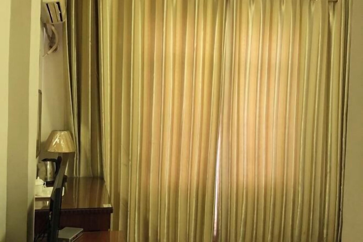 A room with a bed, a nightstand, a lamp, and a curtain.