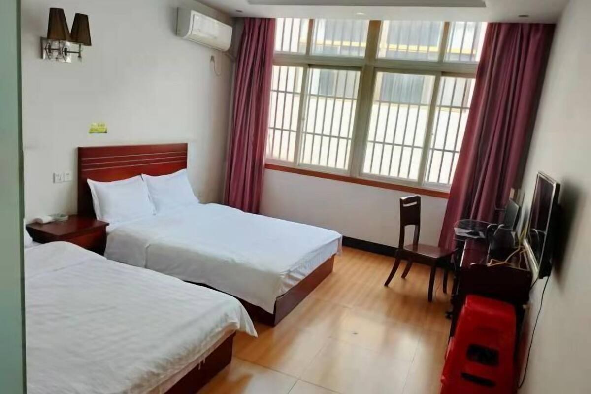 A hotel room with two beds, a desk, a chair, a TV, and a window with curtains.
