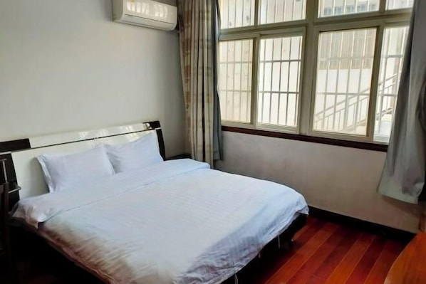 A bed in a room with a window, curtains, and an air conditioning unit.