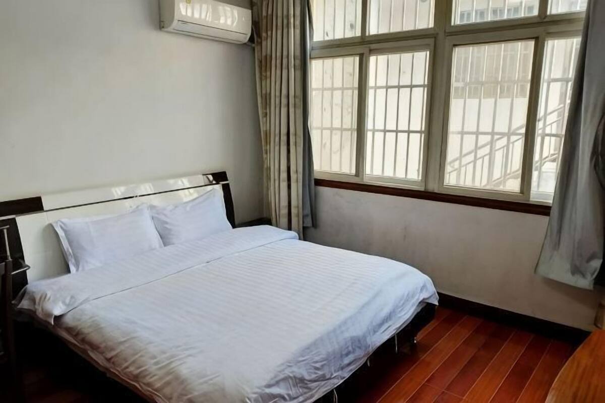 A bedroom with a bed, a window with curtains, and a wooden floor.