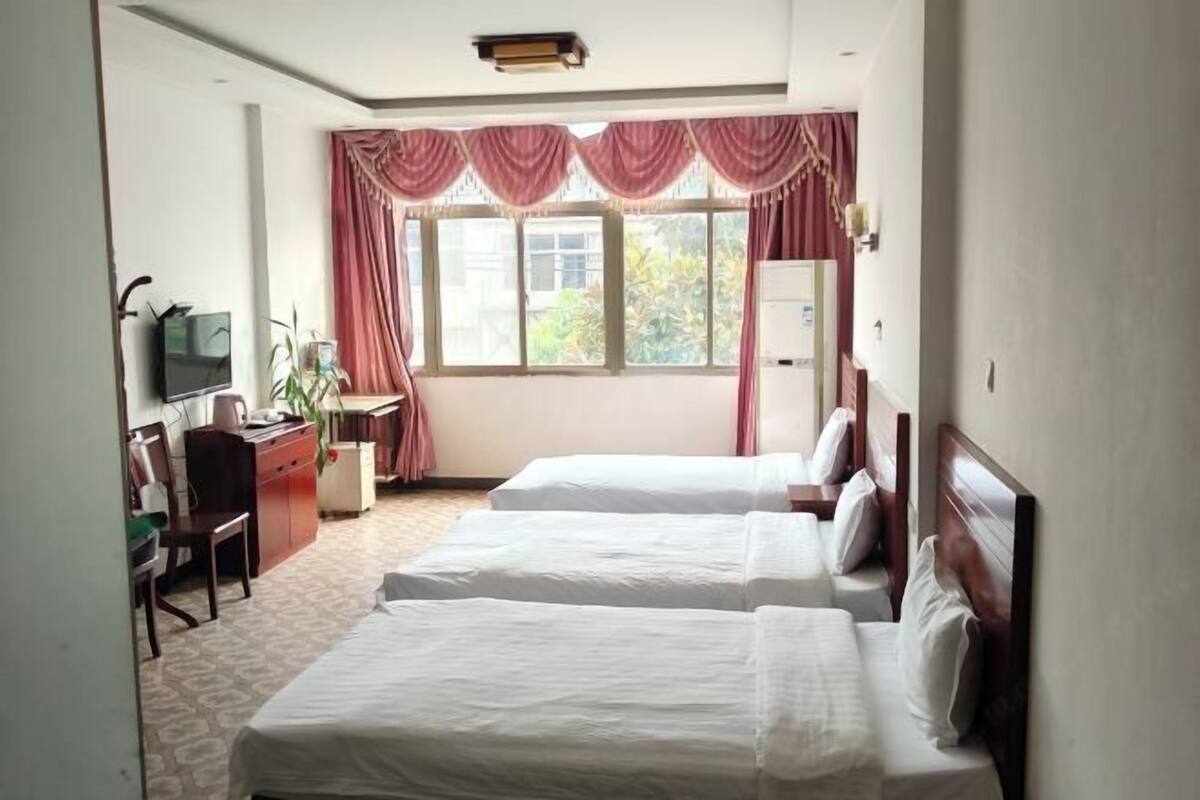 A hotel room with two beds, a desk with a chair, a television, and a window with curtains.