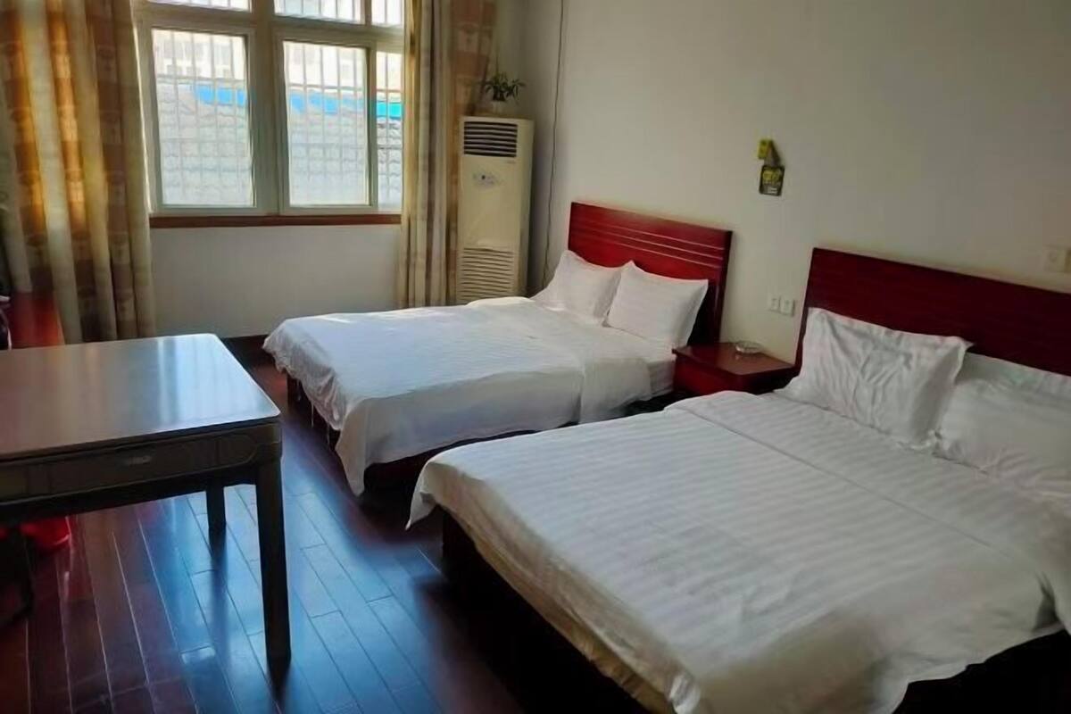 A hotel room with two beds, a table, and a window with curtains.