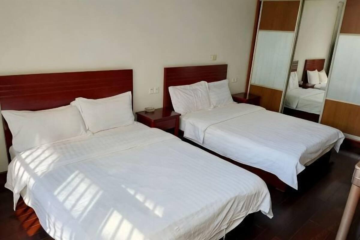 Two single beds with wooden headboards, a nightstand, and a mirror on the wall.