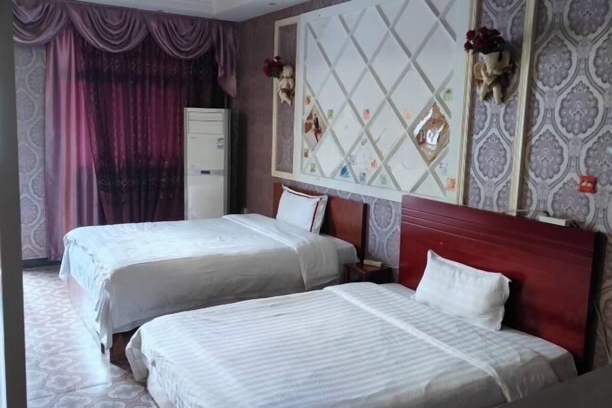 A hotel room with two beds, a wardrobe, a decorative mirror, and patterned wallpaper.
