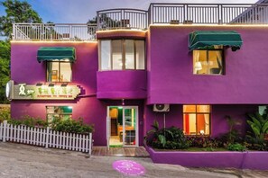 A building with a purple facade, a white picket fence, and a green awning. - Summer Tree Inn (Sanya)