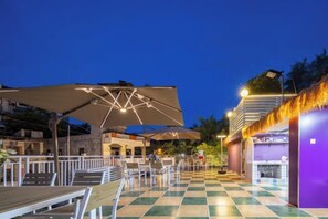 An outdoor seating area with tables and umbrellas, a checkered floor, and a building with a purple facade. - Summer Tree Inn (Sanya)
