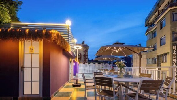 An outdoor dining area with a checkered floor, a round table, and chairs. There is a thatched roof structure and a building in the background. - Summer Tree Inn (Sanya)