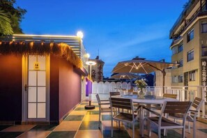 An outdoor dining area with a checkered floor, a round table, and chairs. There is a thatched roof structure and a building in the background. - Summer Tree Inn (Sanya)
