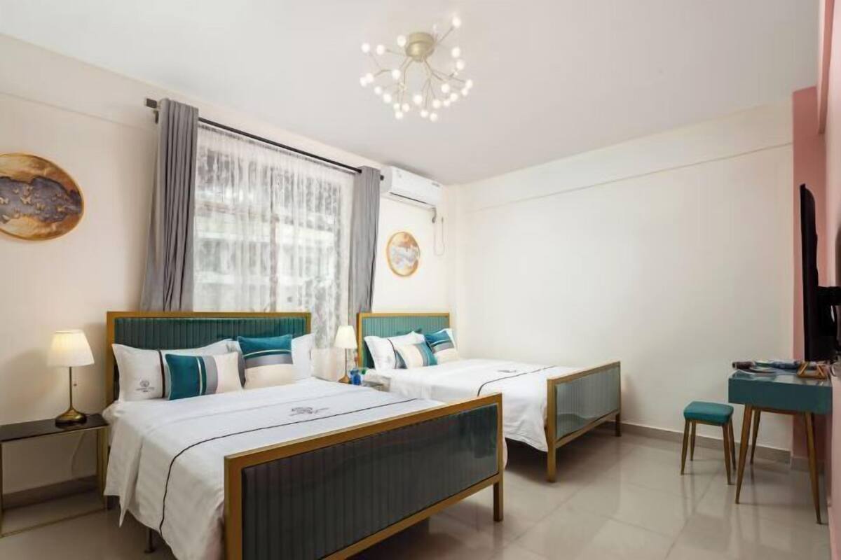 A hotel room with two beds, a desk, a chair, a lamp, and a ceiling light fixture.