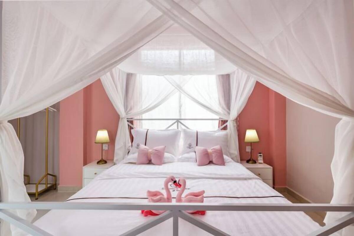A bedroom with a canopy bed, two bedside lamps, and a decorative swan on the bed.