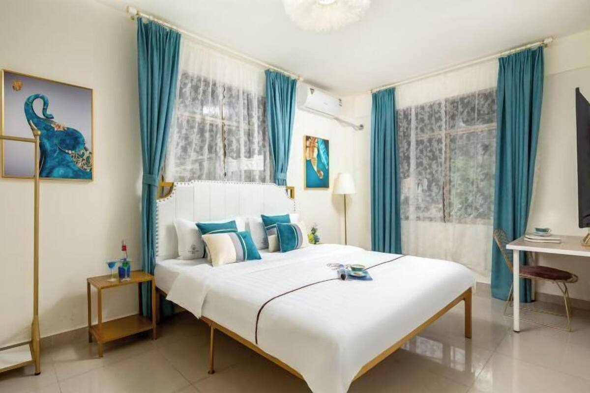 A hotel room with a bed, a desk, a chair, a nightstand, and artwork on the walls.