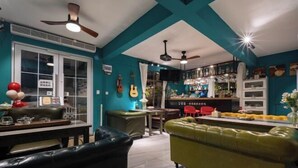 A cozy living room with teal walls, a green sofa, and a bar area with a TV. - Summer Tree Inn (Sanya)