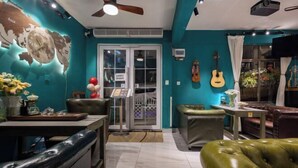 A room with teal walls, a ceiling fan, a projector, a guitar, and a dining area with a table and chairs. - Summer Tree Inn (Sanya)