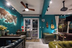 A room with a ceiling fan, a guitar wall decoration, a green sofa, and a dining area with a table and chairs. - Summer Tree Inn (Sanya)