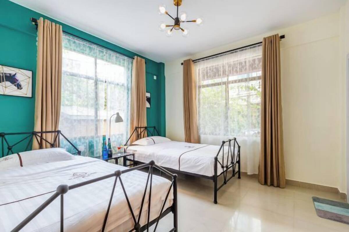 A room with two beds, a ceiling light, and windows with curtains.