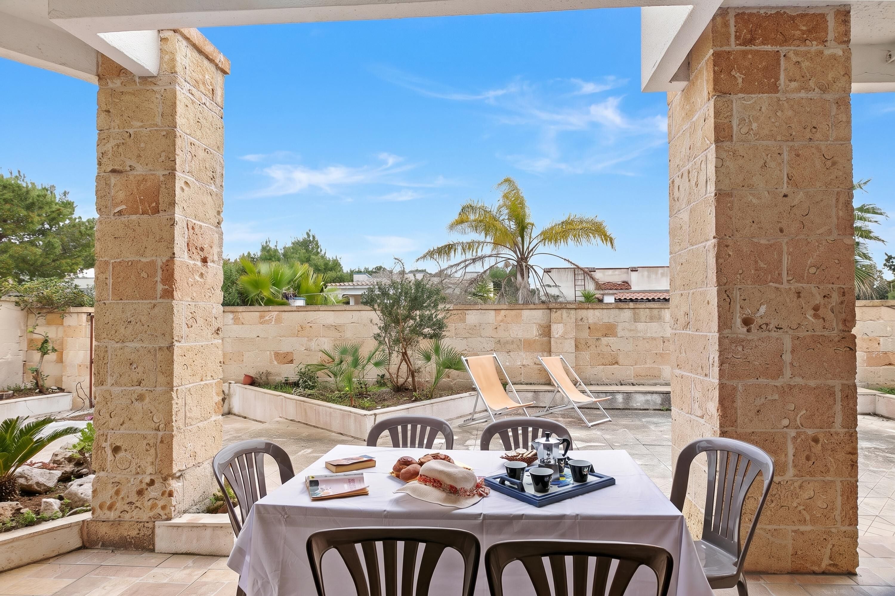 An outdoor dining area with a table set for two, surrounded by stone pillars, under a clear sky.