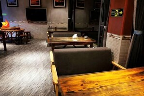 A restaurant interior with wooden tables and chairs, a brick wall, and a flat-screen TV mounted on the wall. - Xiaoluo Ha'ni Titian Sheying Zhijia Hostel (Yuanyang)
