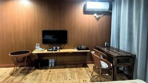 A room with a wooden floor, a TV mounted on the wall, a desk with a chair, and a small table with a chair. - Xiaoluo Ha'ni Titian Sheying Zhijia Hostel (Yuanyang)