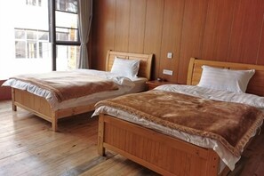 Zwei hölzerne Betten mit weißen Leinentüchern, ein Holzboden und ein Fenster mit Vorhängen.