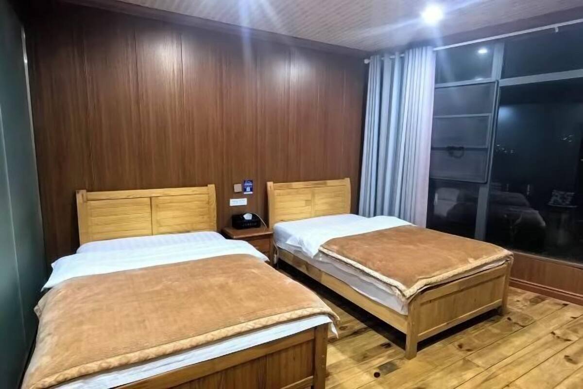 A room with two wooden beds, a nightstand, and a large window with curtains.