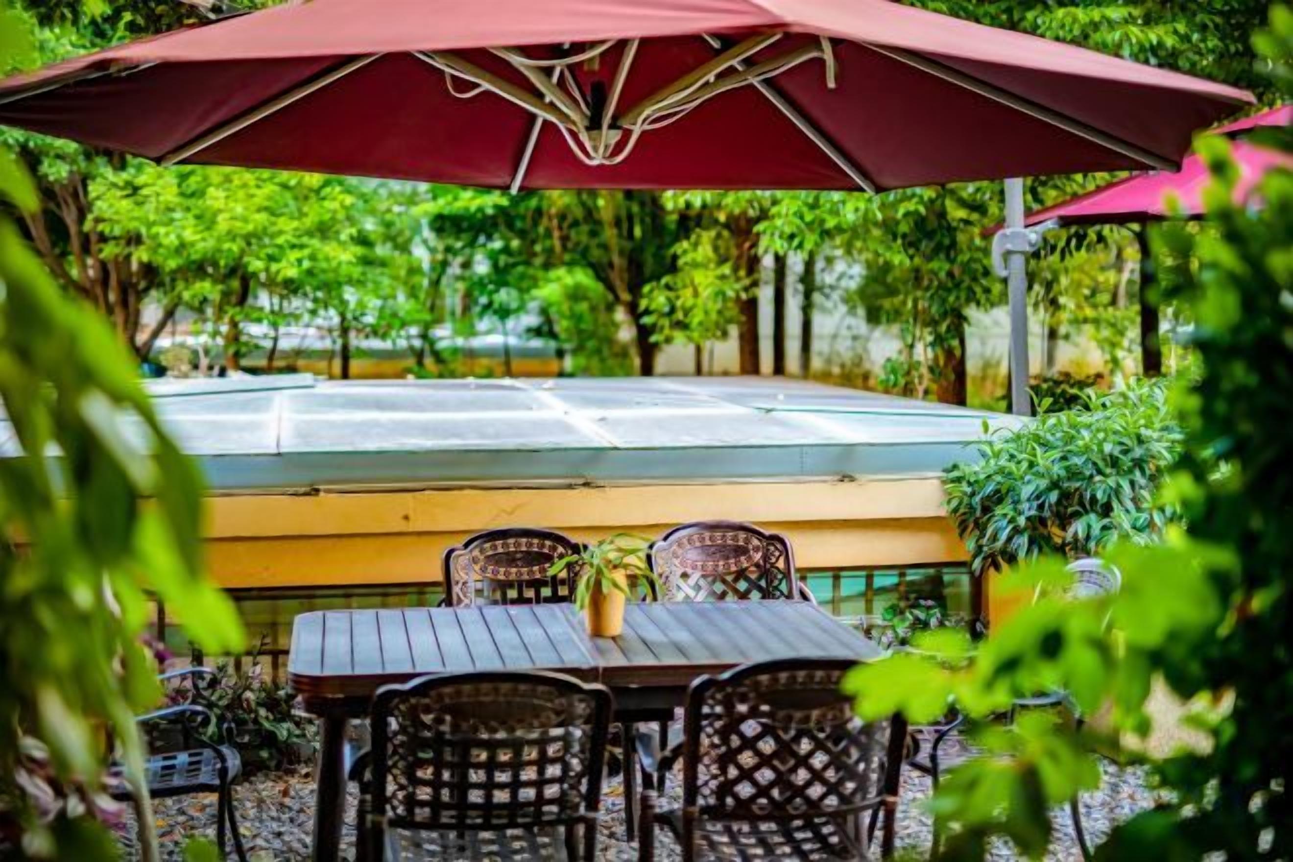 An outdoor seating area with a table and chairs, a large umbrella, and a view of a tennis court.