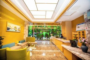 A hotel lobby with a reception desk, seating area, and a view of greenery outside. - Hongting Garden Hotel (Kunming)