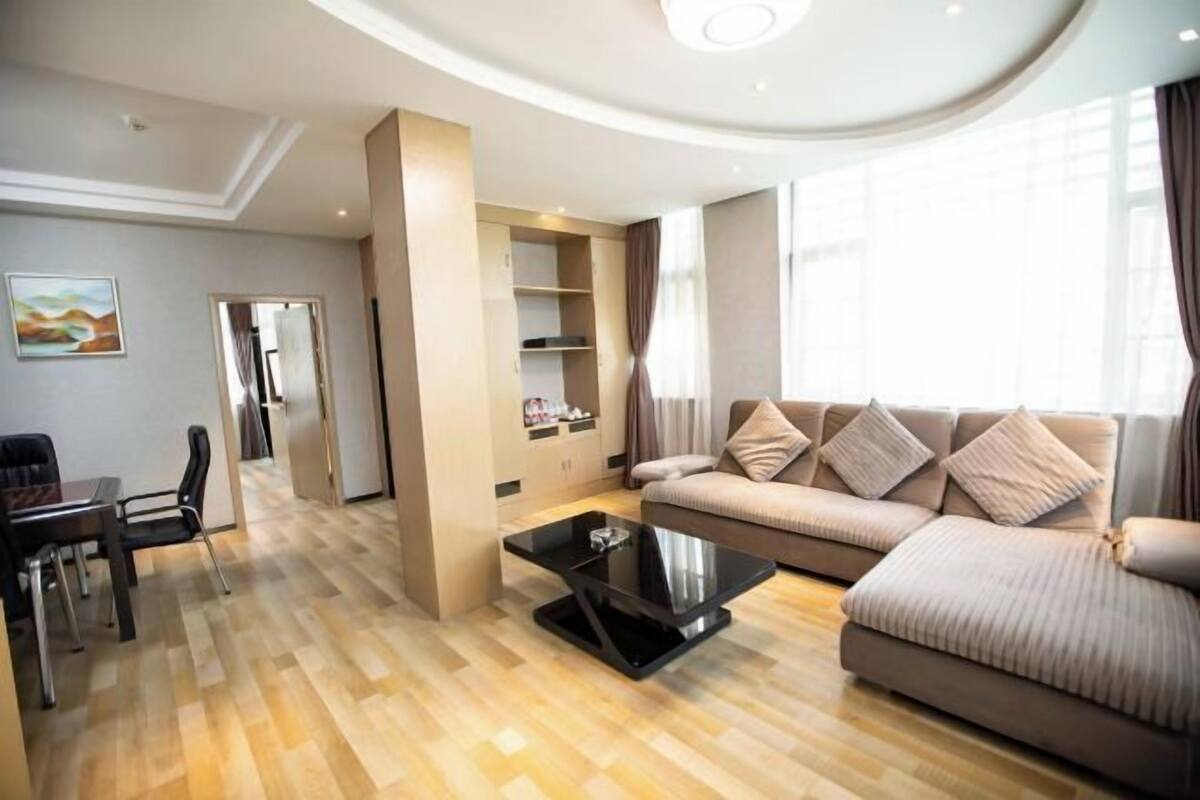 A modern living room with a sofa, a coffee table, a dining area with chairs, and a kitchen area with cabinets.