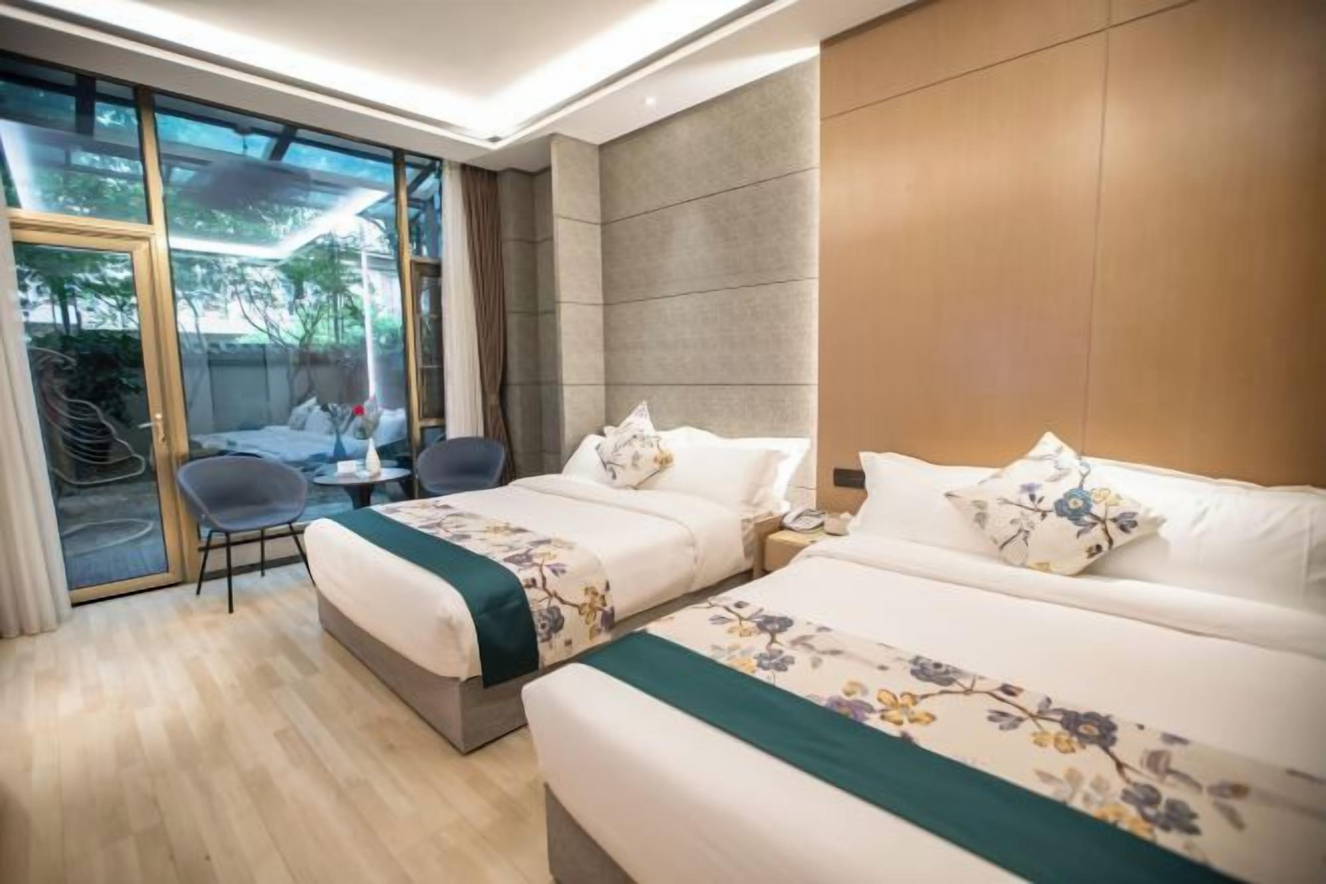 A hotel room with two beds, a seating area, and a view through large windows.