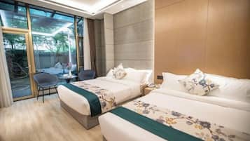 A hotel room with two beds, a seating area, and a view through large windows.