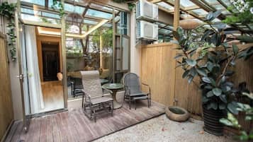 A covered patio with a wooden deck, a glass door leading inside, and a seating area with chairs and a table.