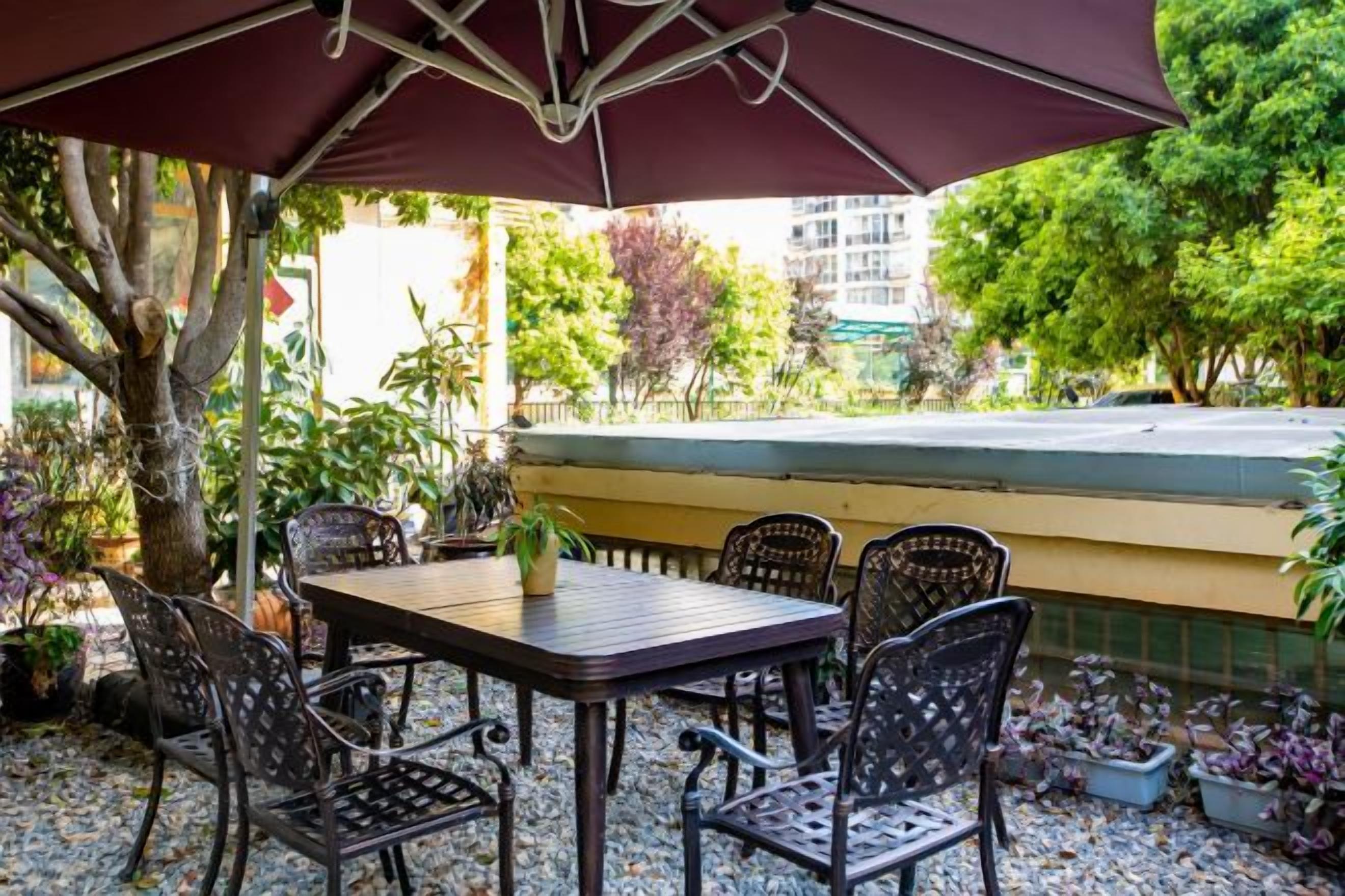 Une terrasse extérieure avec une table et des chaises, entourée de plantes et offrant une vue sur la rue.