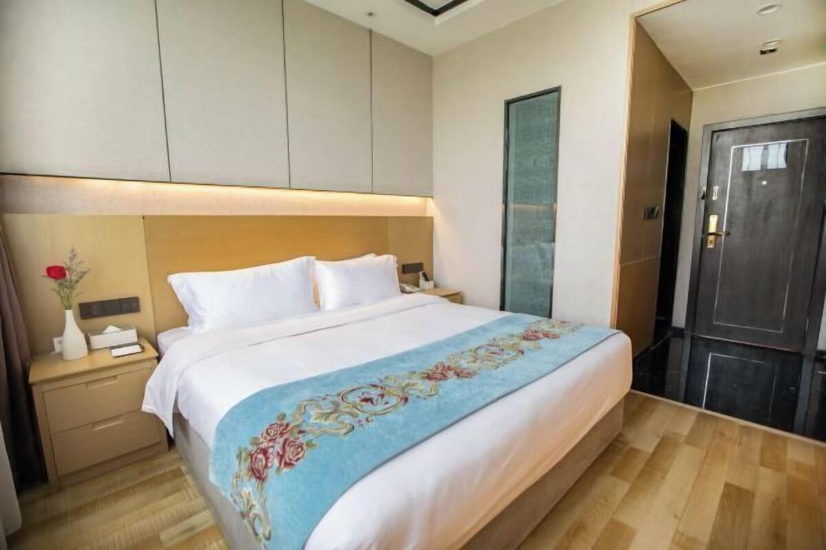 A hotel room with a bed, a nightstand, a dresser, and a door.